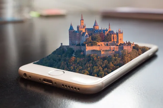 Smartphone on a dark table with a 3D castle on a forested hill rising out of its screen, evoking mobile tour booking