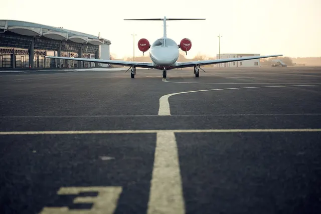Private business jet parked on an airport apron near a terminal building at dusk, with yellow taxiway lines