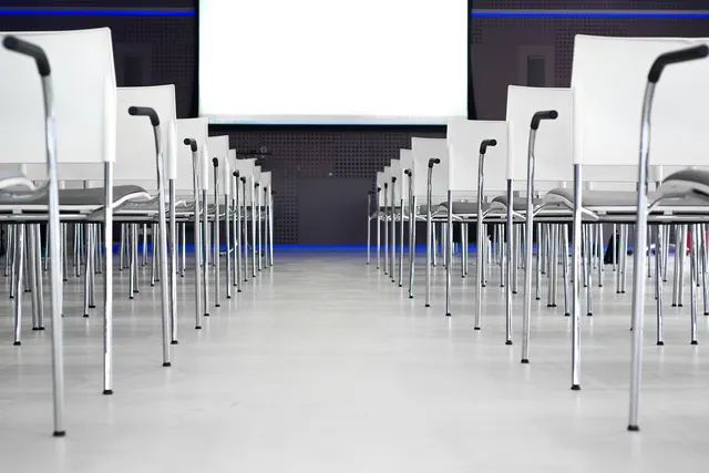 Empty conference room with rows of white chairs facing a blank presentation screen