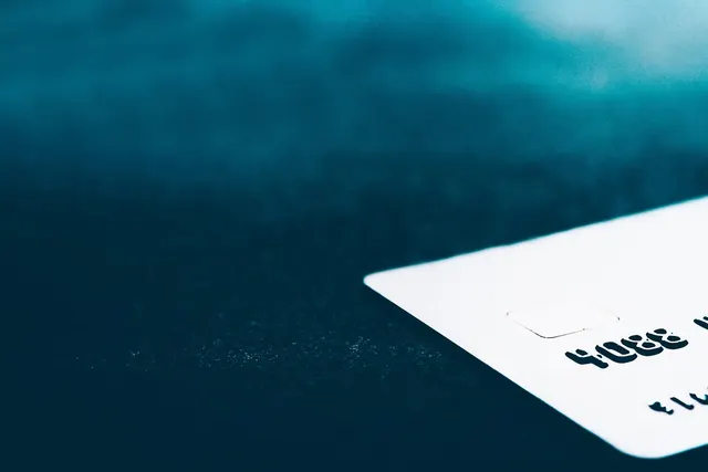 Close-up of a white payment card corner with chip and embossed numbers on a dark teal background