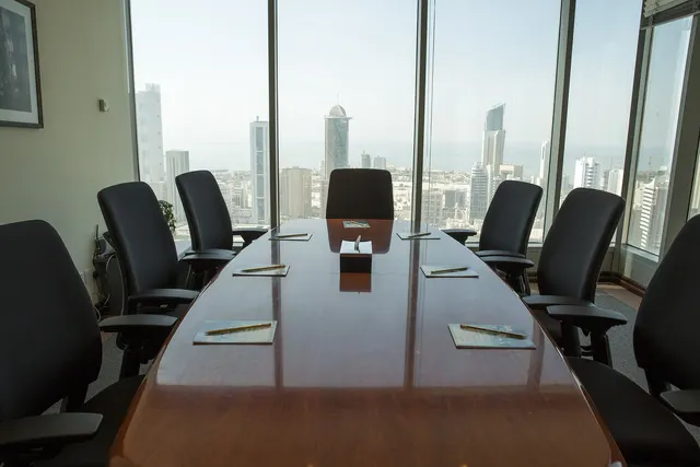 Empty corporate boardroom with polished wooden table, black chairs, notepads and pens, overlooking a city skyline
