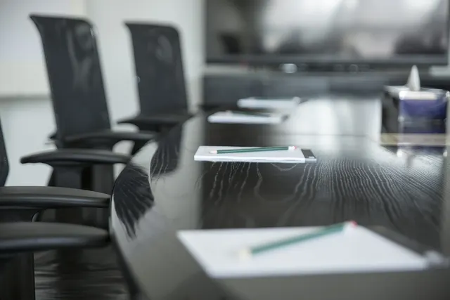 Empty boardroom with black mesh chairs along a glossy dark table set with notepads and green pencils