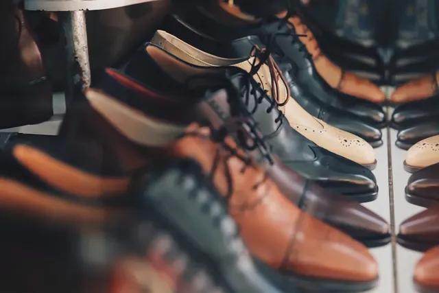 Rows of men's leather dress shoes in brown, black and tan displayed on a boutique shelf beside a mirror