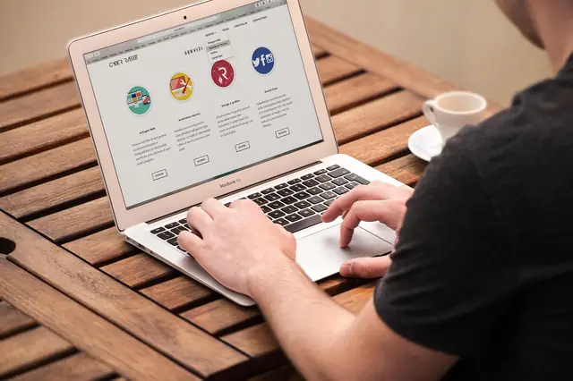 Man typing on a laptop showing a website at a wooden table