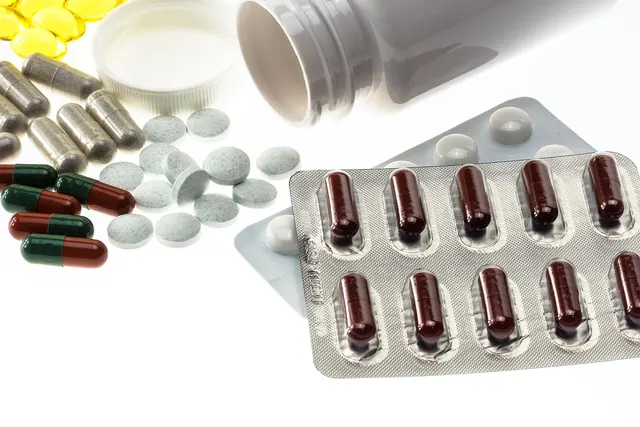 Assorted capsules, tablets and yellow softgels spilling from a white bottle beside a blister pack of brown capsules