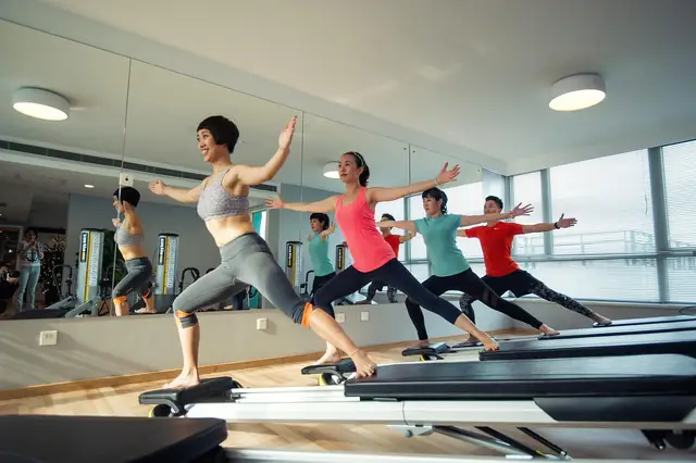 Group exercise class doing lunges on reformer machines in a studio
