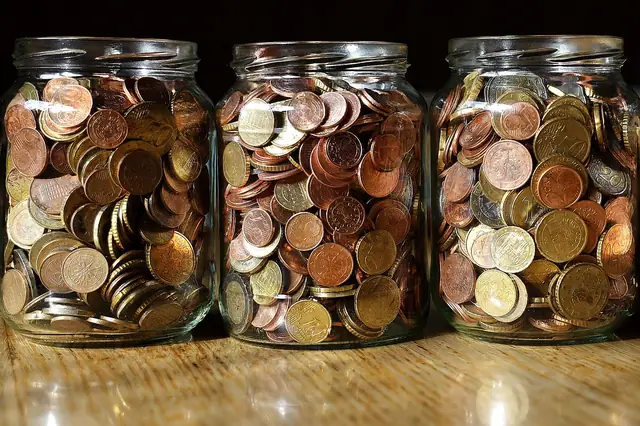 Three glass jars filled with coins on a wooden surface