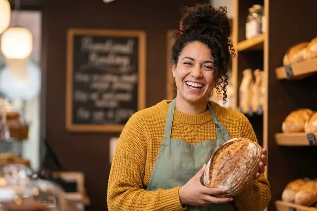 Smiling baker in an apron holding a loaf of bread