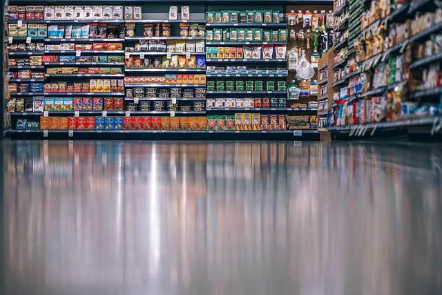 Low-angle view of a store aisle with shelves stocked with packaged products, reflected in a glossy floor