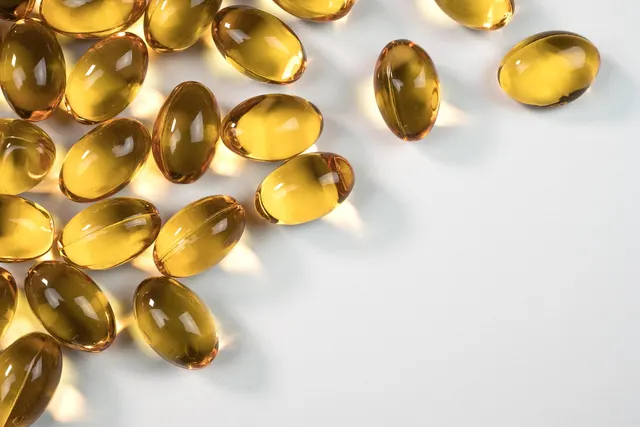 Clear amber softgel supplement capsules scattered across a white surface in soft light