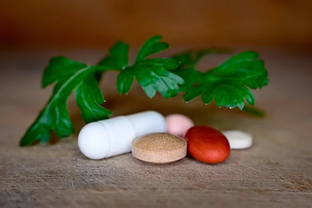White capsule, brown, red, pink and white tablets beside a sprig of green parsley leaves on a wooden surface