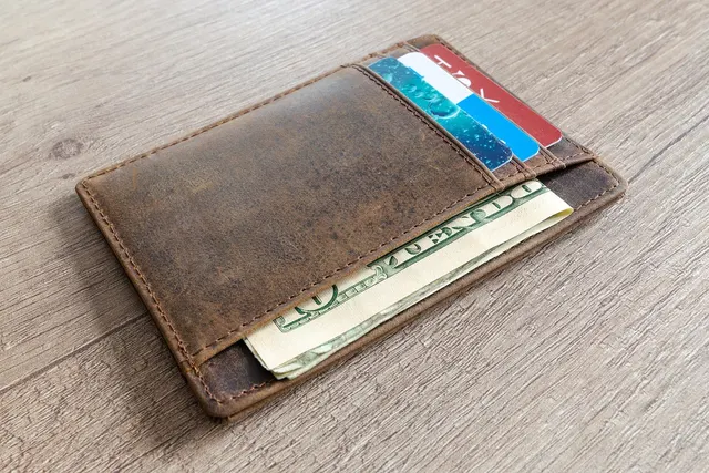 Brown leather card wallet holding several payment cards and folded US dollar bills on a wooden table