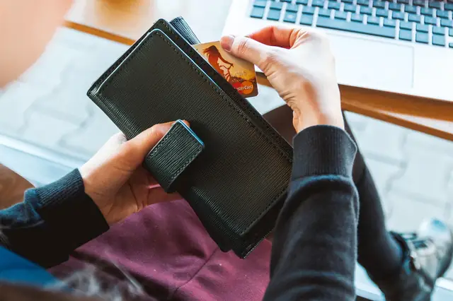 Person taking a card from a wallet in front of a laptop