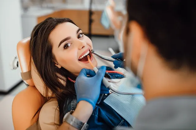 Smiling woman in a dental chair as a dentist in blue gloves examines her teeth with dental instruments