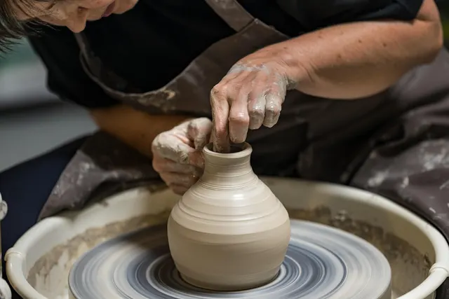 Potter in a clay-stained apron shaping a ceramic vase on a spinning pottery wheel with clay-covered hands