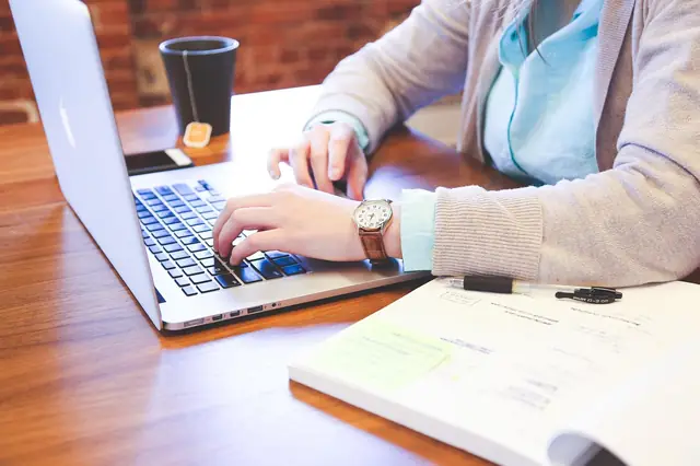 Person typing on a laptop beside an open notebook
