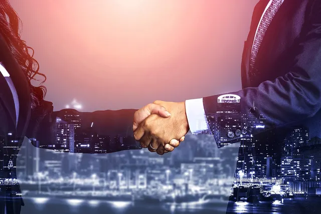 Businesswoman and businessman in suits shaking hands, double-exposed over a night city skyline