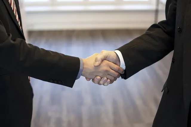 Close-up of two businesspeople in dark suits shaking hands in a bright office with wooden floors